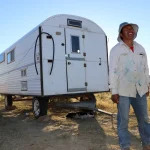 A sheepherder in Utah stands outside his mobile housing unit